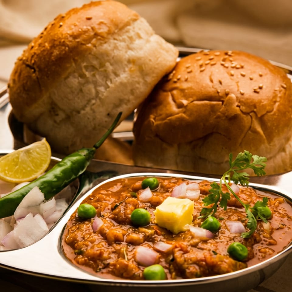 Indian pav bhaji served with buttered buns, green peas, chopped onions, cilantro, lime, and green chili on a metal platter.